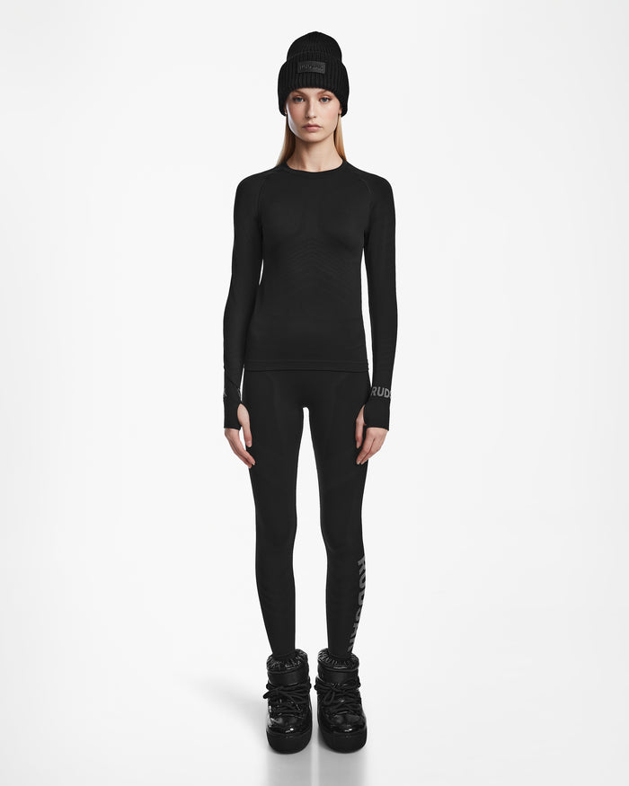 A woman faces forward in an all-black Rudsak CARRIE - 8524619 womens thermal set—beanie, long-sleeve shirt, stretch leggings, and winter boots—against a plain white background.