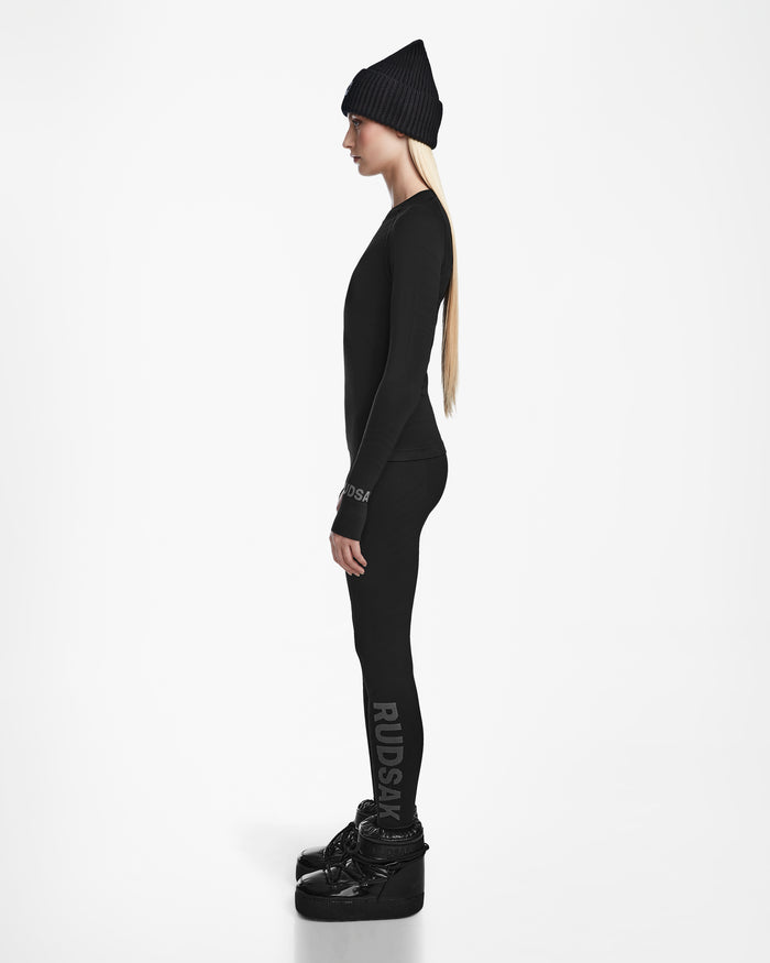 A woman in a black beanie, Rudsak’s CARRIE - 8524619 Black thermal set and stretch leggings stands in profile against a white background, wearing black platform shoes and RUDSAK branding on her sleeve and leg.