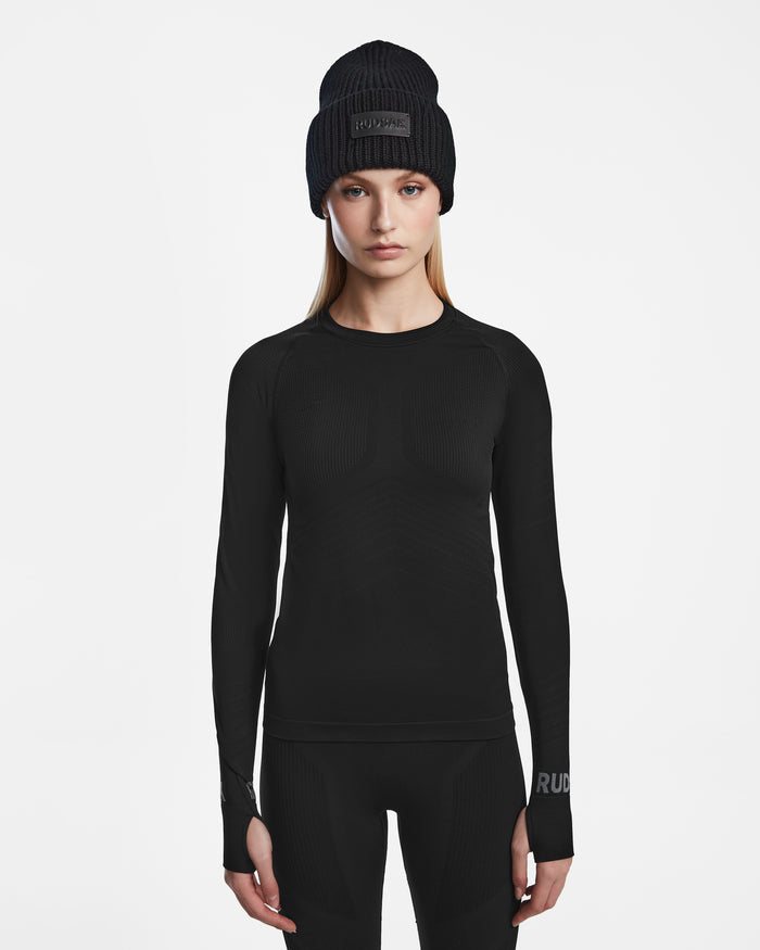 A woman faces forward in a Rudsak CARRIE - 8524619 Black knit beanie and fitted black athletic top with long sleeves and thumbholes, ideal as a women’s thermal set or ski base layer. The background is plain white.