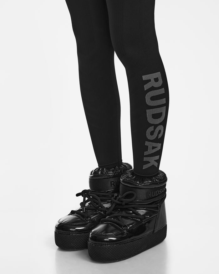 The CARRIE - 8524619 Black high-top sneakers by Rudsak, featuring black stretch leggings with “RUDSAK” boldly printed down the side, are shown against a plain white background.