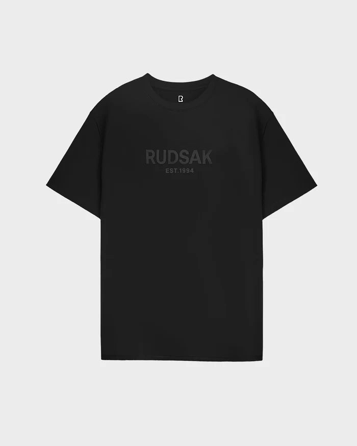The Rudsak CASEY - 6525037 Black short-sleeve mens T-shirt features RUDSAK EST.1994 in dark print across the chest and is displayed on a plain white background—a timeless classic for any wardrobe.