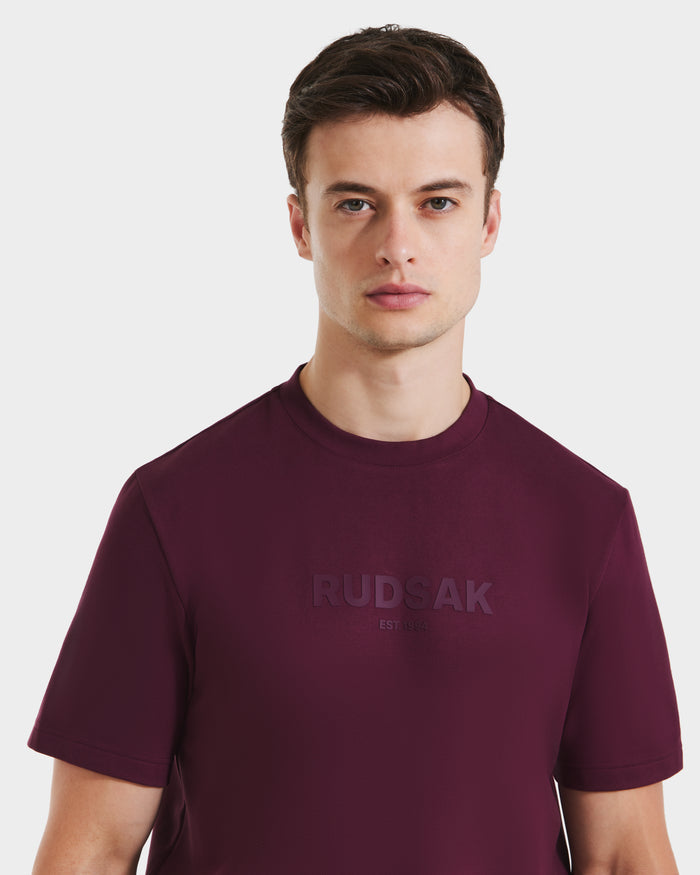 A man with short brown hair wears the Rudsak CASEY - 6525037 Bordeaux T-shirt, featuring embossed "EST. 1994" on the chest, standing against a plain white background.