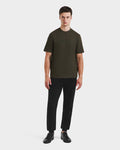 A man faces forward against a plain white background, wearing the Rudsak CASEY - 6525037 dark olive T-shirt with black pants and black sneakers.