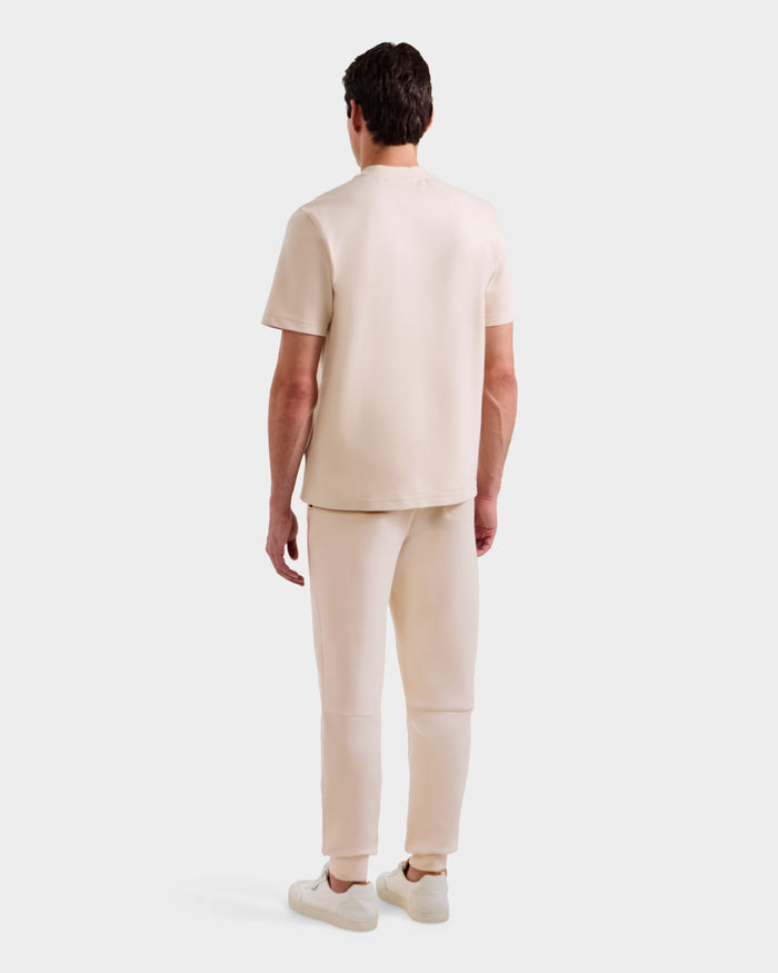 A person stands facing away from the camera, wearing the Rudsak CASEY - 6525037 Vanilla mens T-shirt and pants with white sneakers, set against a plain white background.