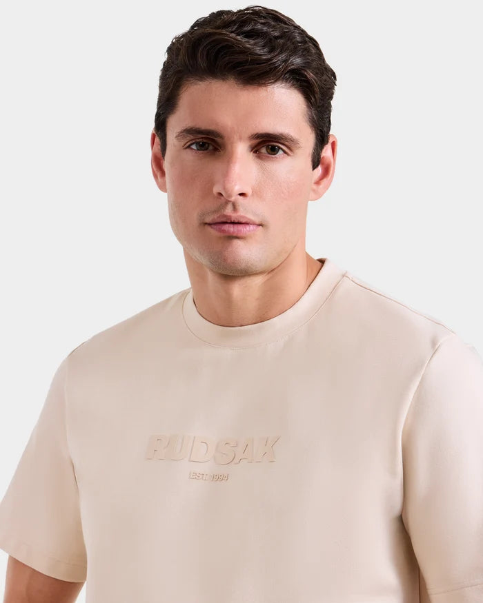 A man with short brown hair models the Rudsak CASEY - 6525037 Vanilla T-shirt, an effortlessly comfortable mens essential, as he looks directly at the camera against a plain light background.