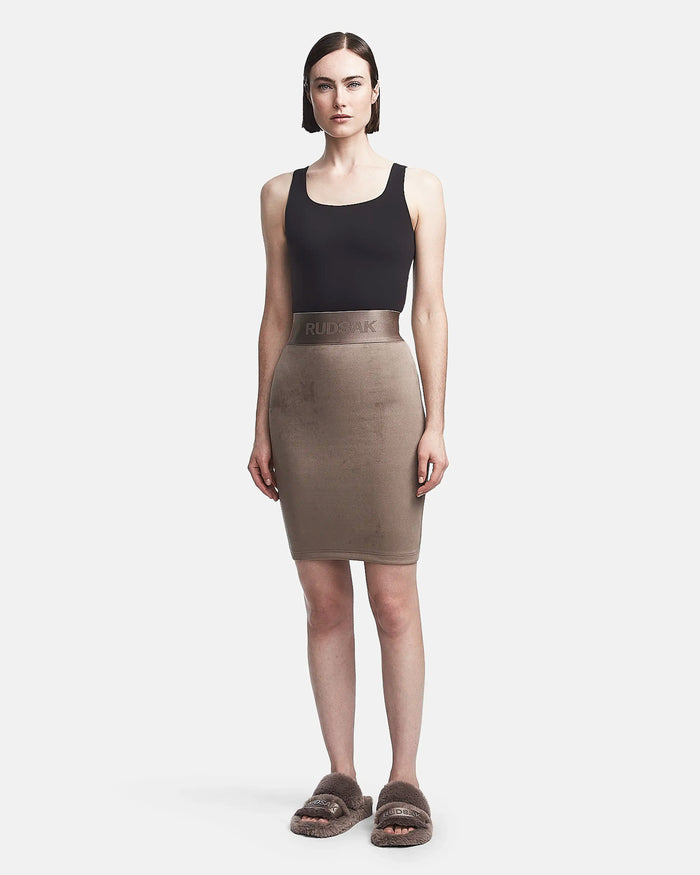 A woman faces forward in a black sleeveless crop top and the CHEYNA - 8523514 Cement womens faux suede pencil skirt by Rudsak, featuring a branded waistband. She completes her look with brown fuzzy slide sandals against a white background.