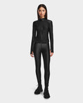 A woman faces forward, wearing Rudsaks CLARE - 8524519 Black fitted zip-up jacket and matching shiny stretch leggings with black boots, against a plain white background that highlights her sculpted silhouette.