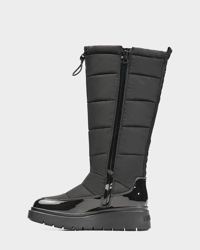The Rudsak CLAUDE - L223506 Black is a women’s mid-calf quilted winter boot with shiny patent accents, a drawstring top, side zipper, and thick ridged sole—perfect waterproof protection for harsh weather.