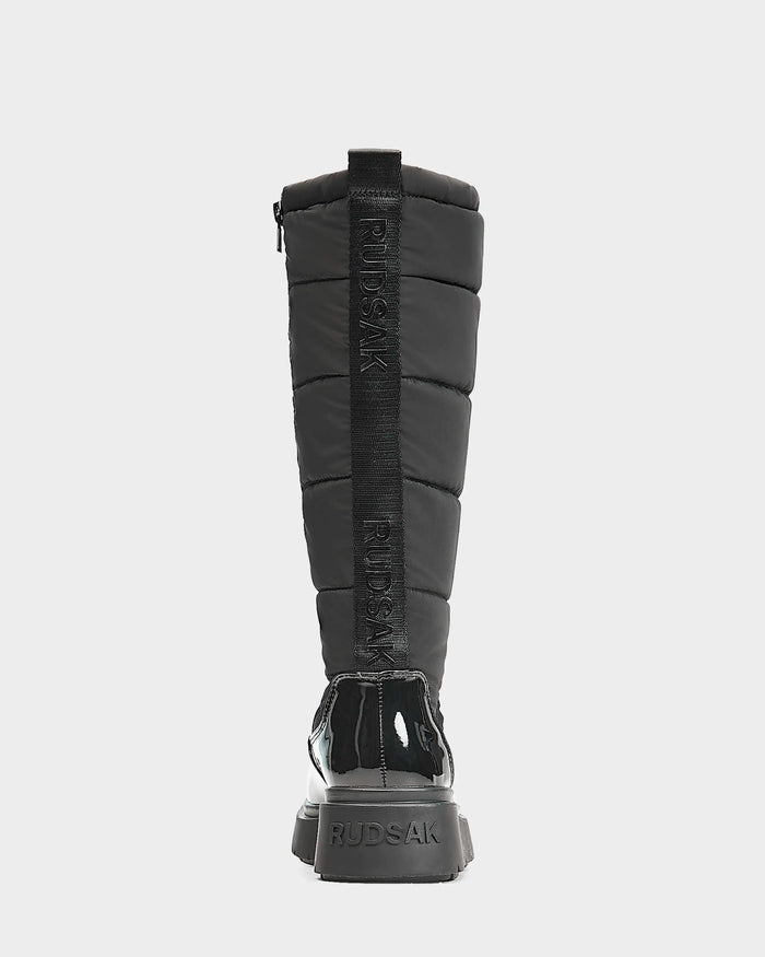 The Rudsak CLAUDE - L223506 Black is a womens tall quilted winter boot with padded sections, a vertical pull tab featuring RUDSAK CLAUDE branding, and a chunky sole—ideal as stylish, waterproof winter boots.