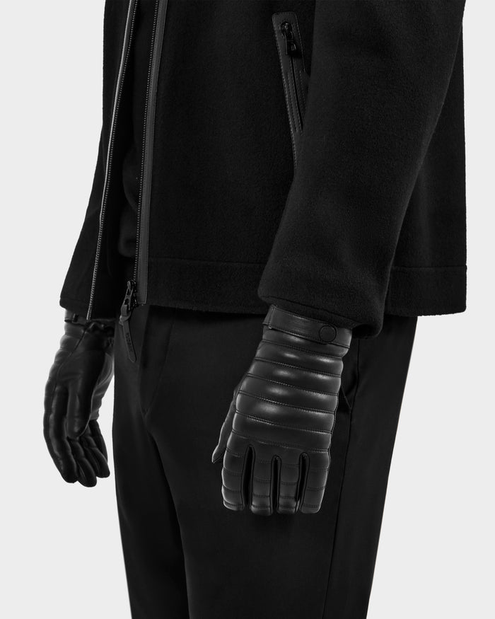 A person stands against a plain light background, wearing black pants and a black CORTES - 6425036 jacket by Rudsak, paired with leather gloves featuring stitched detailing. The image is cropped to show the lower torso, hips, and hands.