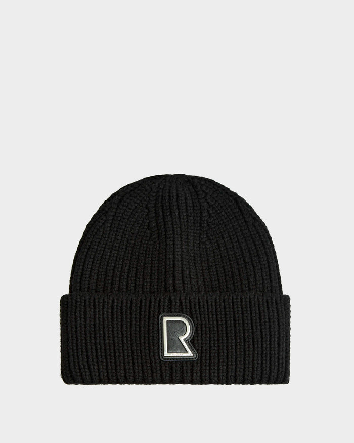 The Rudsak CYBELLE - 9424504 Black/Silver beanie is a unisex wool blend hat with ribbed knit, folded brim, and an embroidered R patch on the front, shown against a plain white background.