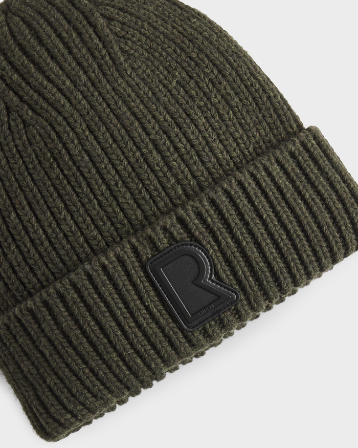 A close-up of Rudsaks CYBELLE - 9424504 Dark Olive ribbed wool blend beanie, featuring a black patch with a raised R on the folded brim—this unisex knit hat blends comfort and style.