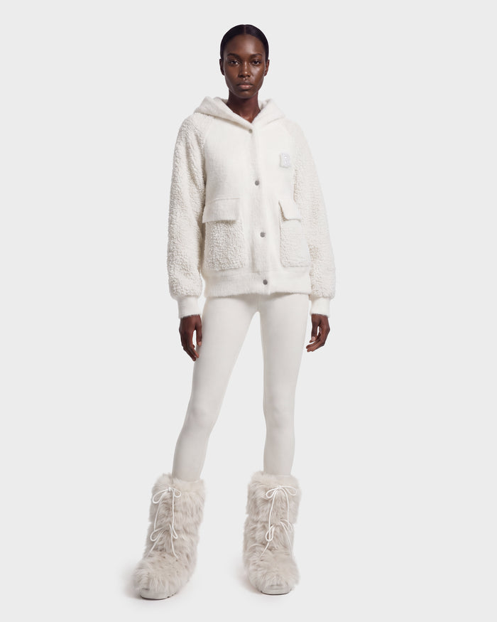 A person stands against a plain light background wearing the Rudsak DAKOTA - 8526515 Iceland cozy white sherpa hoodie, paired with white leggings and fluffy white boots.