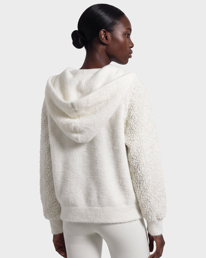 A woman with dark hair in a low bun is shown from behind against a plain light gray background, wearing the Rudsak DAKOTA - 8526515 Iceland textured white hooded jacket and white pants.