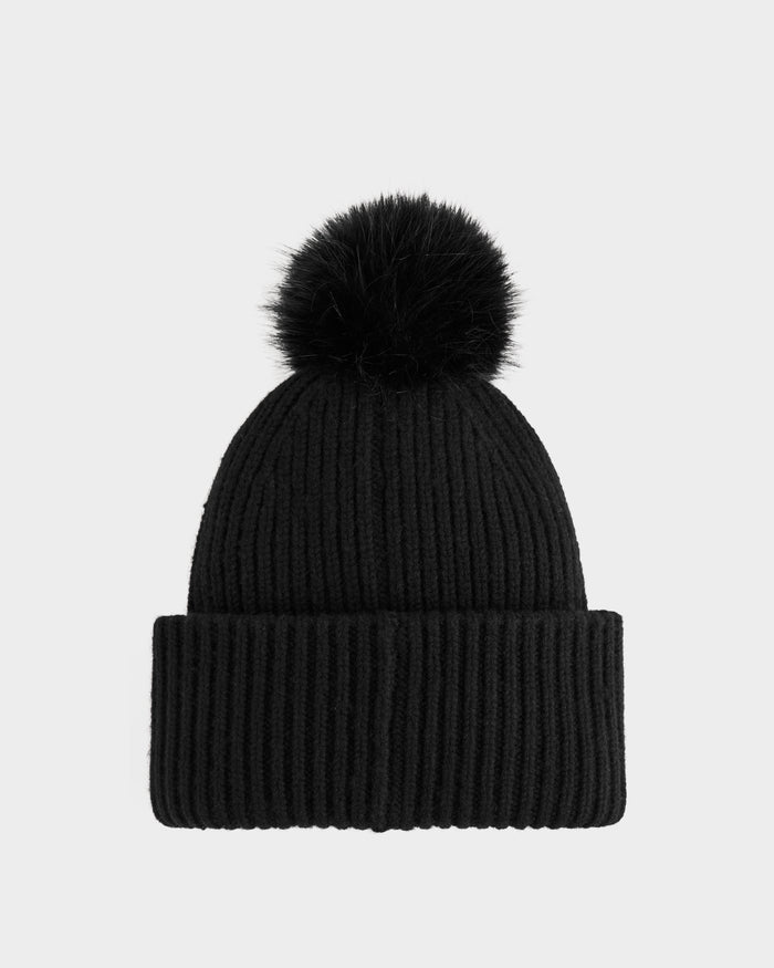 The DARA - 8425019 Black by Rudsak is a black, ribbed knit women's winter hat with a large black faux fur pom pom on top, displayed against a plain light gray background.