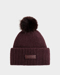 The Rudsak DARA - 8425019 Bordeaux is a women's dark burgundy ribbed knit beanie with a folded brim, faux fur pom-pom, and front brown leather patch embossed with RUDAK. Shown on a plain light gray background.
