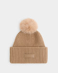 The DARA - 8425019 Camel by Rudsak is a women’s tan ribbed knit tuque made from a cozy cashmere wool blend. It features a large, fluffy faux fur pom pom on top and a folded brim with a rectangular patch embossed with the Rudsak logo, shown against a plain white background.