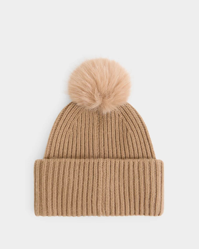 The DARA - 8425019 Camel women’s tuque by Rudsak is crafted from a soft cashmere wool blend in tan, featuring a folded brim and topped with a large, fluffy faux fur pom pom, displayed on a plain white background.