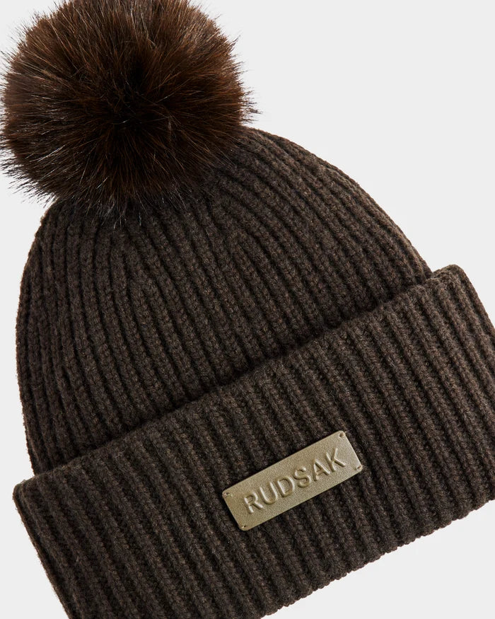 The DARA - 8425019 Dark Olive by Rudsak is a ribbed knit beanie featuring a large faux fur pom pom, folded brim, and rectangular RUDSAK label—an essential for stylish warmth all season.