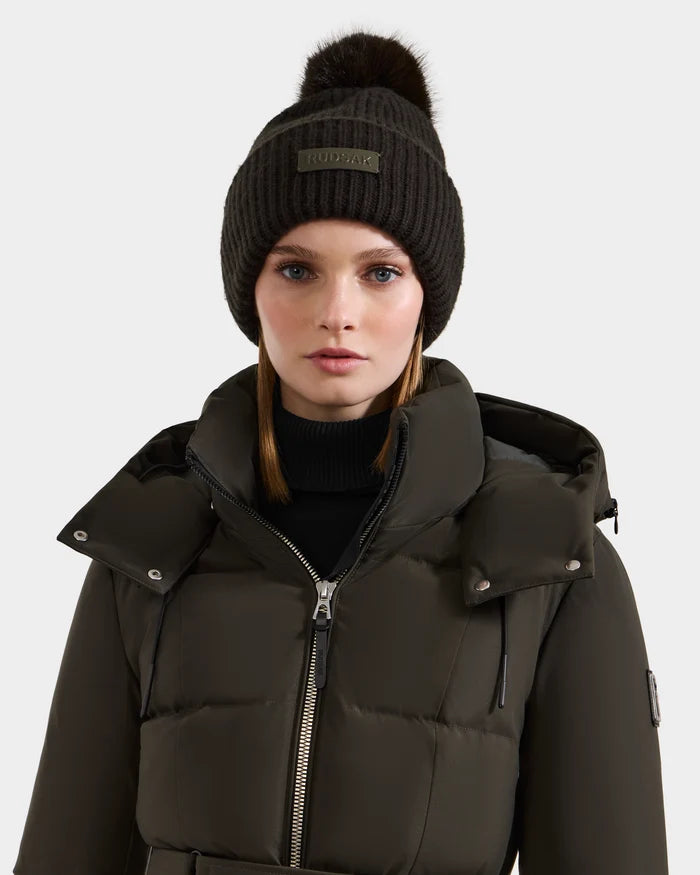 A woman stands facing forward against a plain light background, wearing the Rudsak DARA - 8425019 Dark Olive puffer jacket and a dark knit tuque with a faux fur pom pom.