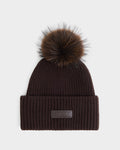 The DARA - 8425019 Espresso by Rudsak is a dark brown ribbed knit women’s winter hat, featuring a wide folded brim, a large faux fur pom-pom on top, and a rectangular leather patch with embossed branding on the front.