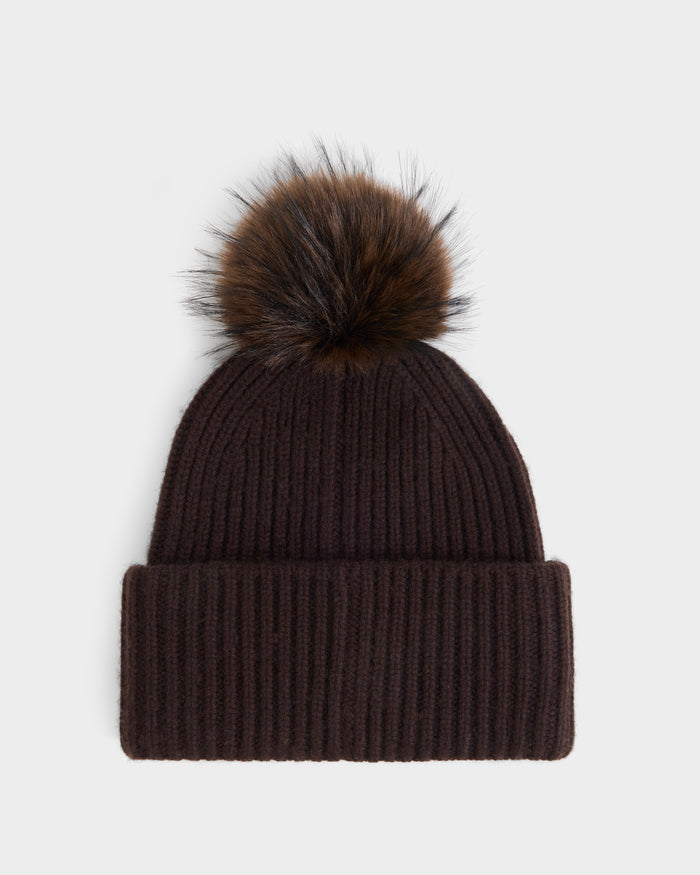 Introducing the DARA - 8425019 Espresso by Rudsak, a chic women’s winter hat in dark brown ribbed knit, featuring a folded brim and an oversized faux fur pom pom. Crafted for both warmth and style, this cashmere wool tuque brings cozy elegance to any cold-weather outfit—your ideal accessory for the season. Shown against a crisp white background, it’s the perfect blend of comfort and sophistication.