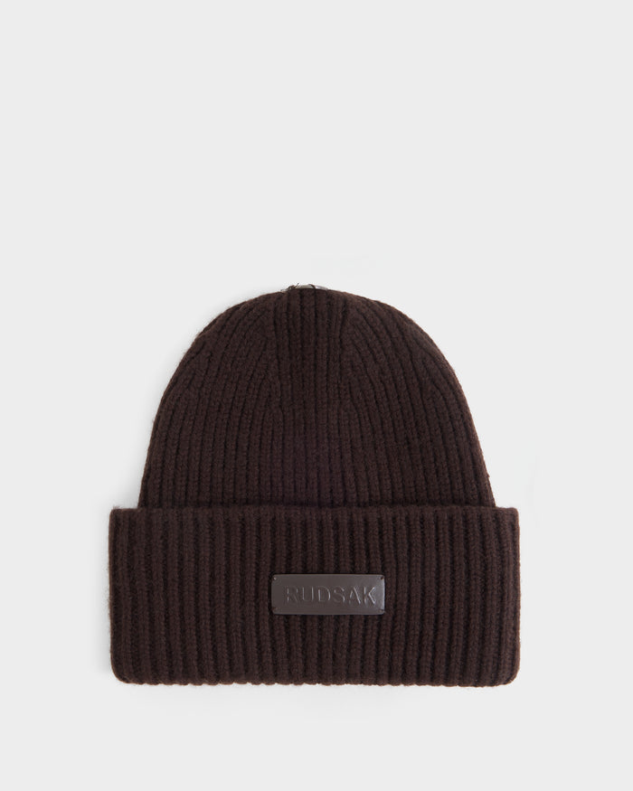 Here’s a revised version of your sentence using the provided product data: The DARA - 8425019 Espresso is a women’s winter hat by Rudsak, featuring a ribbed knit construction in espresso with a folded brim and a rectangular Rudsak logo patch on the front, displayed on a white background.