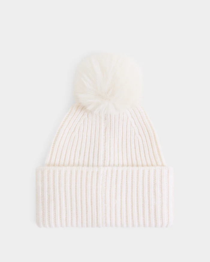 The DARA - 8425019 Vanilla by Rudsak is a women’s white ribbed knit tuque featuring a folded brim and a large, fluffy faux fur pom pom on top. Crafted from a soft cashmere wool blend, it is shown against a plain white background.