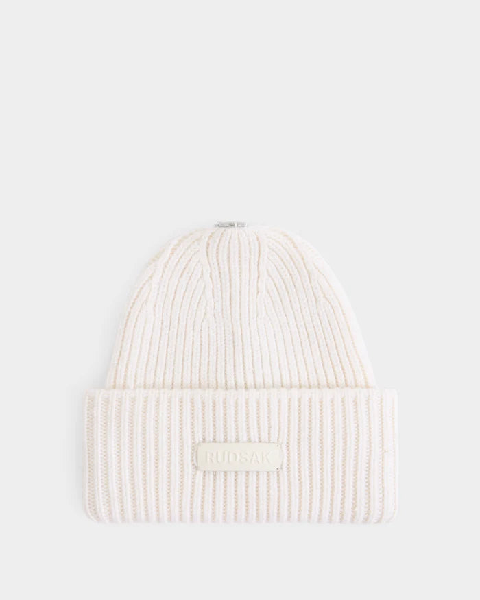 A women’s tuque named DARA - 8425019 Vanilla by Rudsak, crafted from a soft cashmere wool blend in a cream hue, features ribbed knitting, a folded brim, and a rectangular front patch displaying the Rudsak brand name. The tuque is presented against a plain white background.