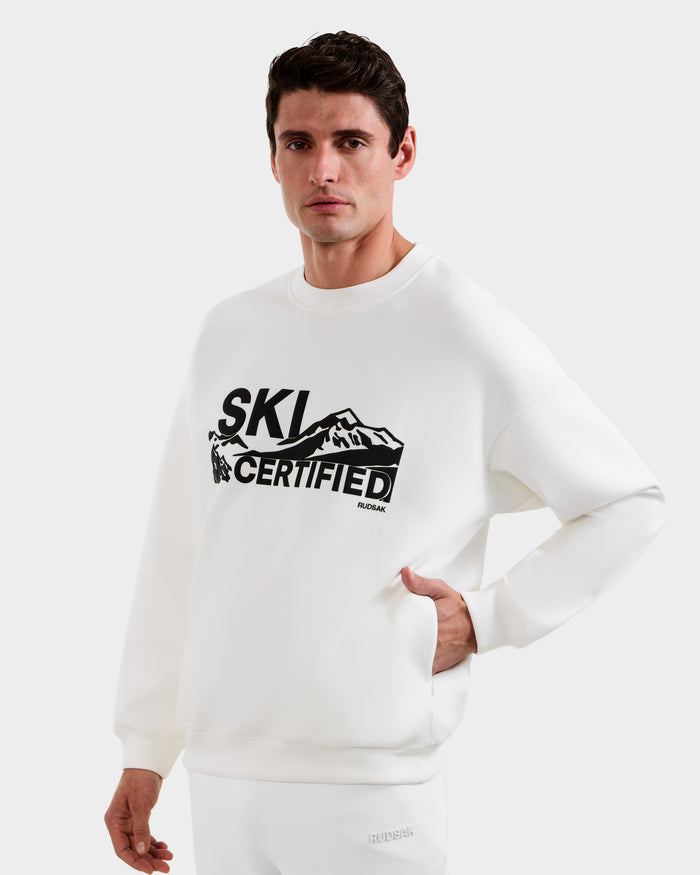 A man stands against a plain white background wearing the Rudsak DECLAN - 6525648 Iceland men’s crewneck sweatshirt featuring "Ski Certified" and a mountain graphic printed in black on the front.