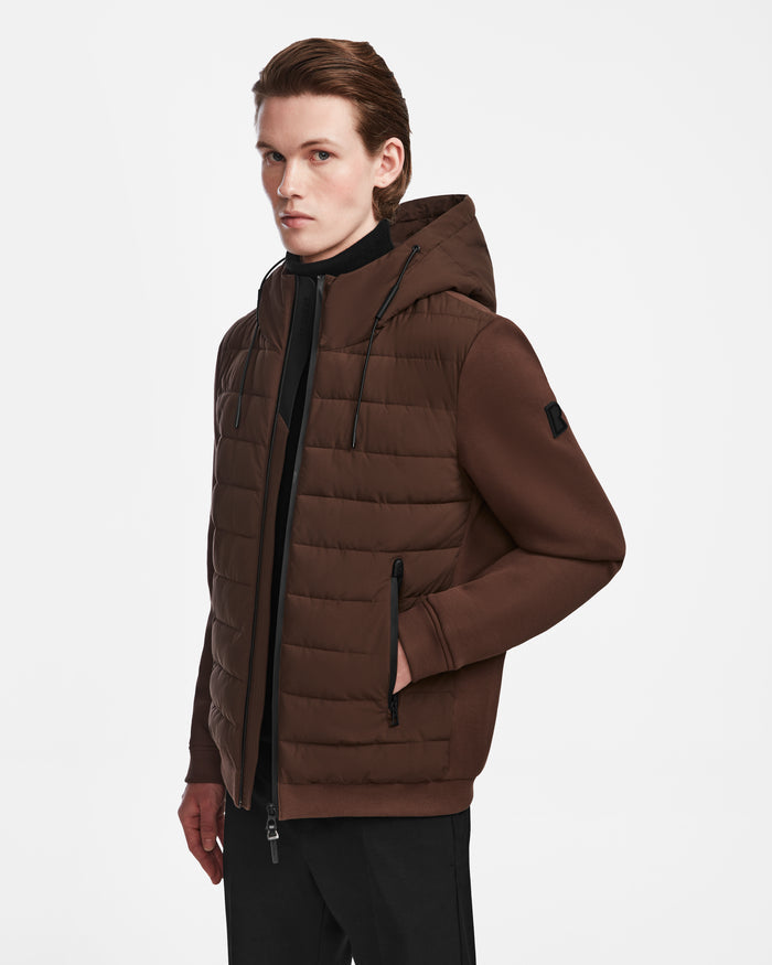 A person with slicked-back hair models the Rudsak ELIAS - M124002 Espresso men’s quilted light jacket, featuring a water-resistant shell and zippered pockets, paired with black pants against a plain white background.