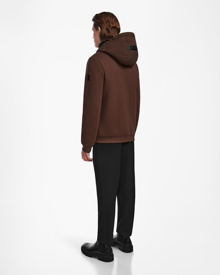 A person with medium-length brown hair, facing away, wears the Rudsak ELIAS - M124002 Espresso men’s quilted jacket with black pants and black shoes against a plain white background.