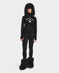 A person stands facing forward in the Rudsak ELIZABETH - 8524623 Black womens ski turtleneck with white symbols, paired with black leggings and matching furry accessories, all set against a plain white background. Ideal for any winter wardrobe.