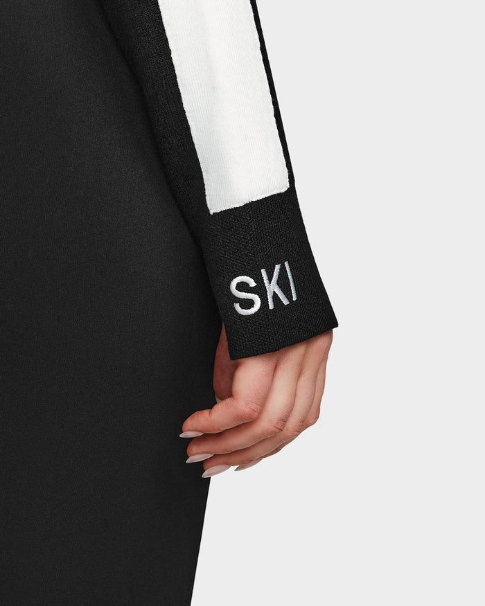 A close-up of a hand resting on the black sleeve with a white stripe of the Rudsak ELIZABETH - 8524623 womens ski turtleneck, featuring SKI embroidered in white—an essential winter piece. The background is plain and light-colored.