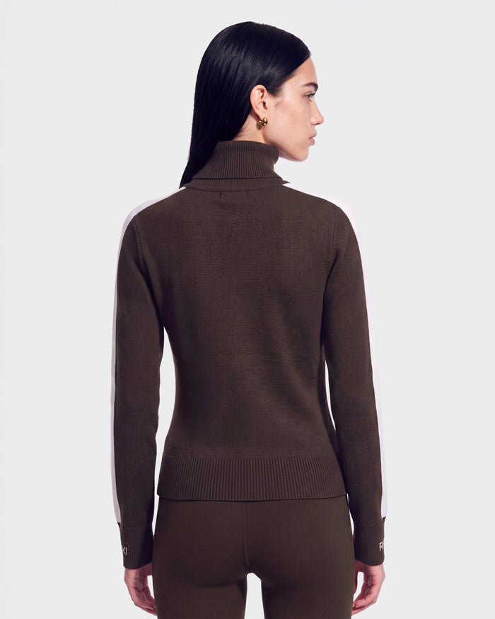 A woman with long dark hair, wearing the Rudsak ELIZABETH - 8524623 Espresso women’s ski turtleneck sweater and matching pants, stands facing away from the camera against a plain light background—a stylish choice for any winter wardrobe.
