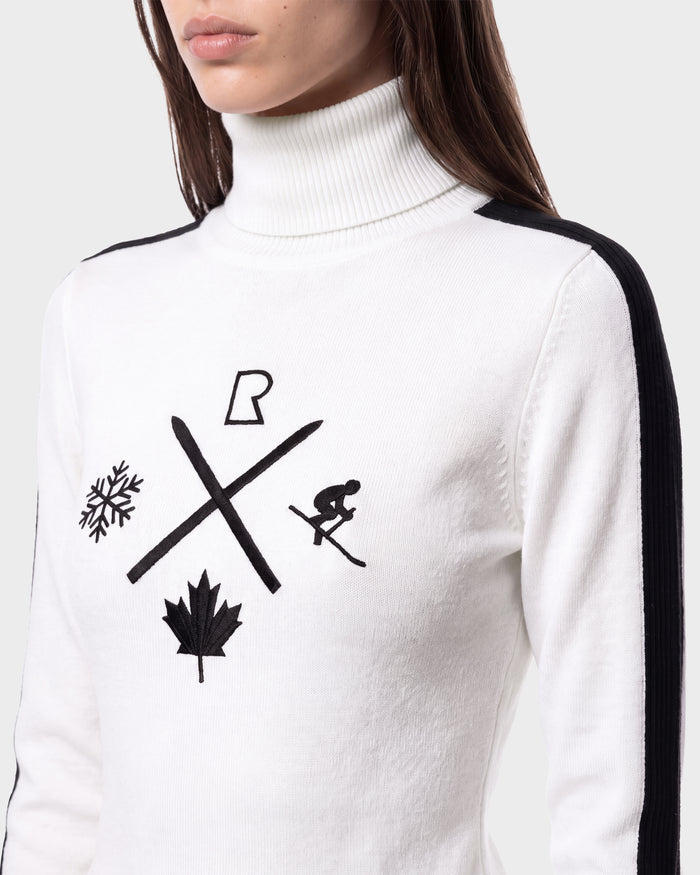 A woman wearing the Rudsak ELIZABETH - 8524623 Optic White ski turtleneck, adorned with black icons—including a snowflake, maple leaf, crossed skis, skier, and a stylized R—embodies classic après-ski style. This white sweater, detailed with bold black stripes on the shoulders and sleeves, is an essential addition to any winter wardrobe.
