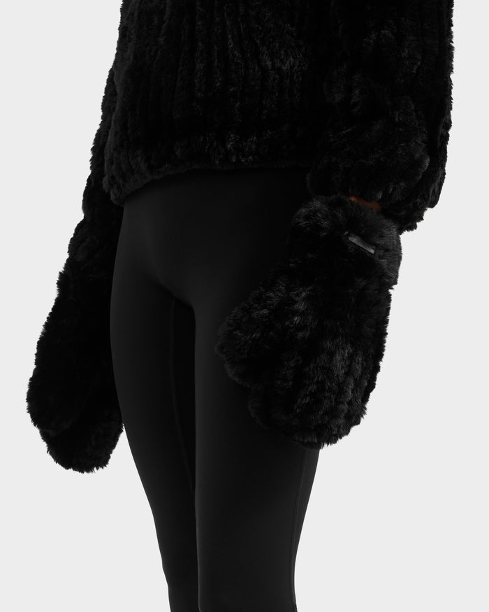 A person is seen from the waist down against a plain light background, wearing Rudsak's ELOISE - 8425559 Black faux fur mittens, a black fuzzy sweater, and black leggings as winter essentials.