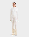 A woman stands facing forward, wearing the Rudsak ERIKA - 8523536 Iceland turtleneck, fitted pants, fluffy earmuffs, and chunky snow boots—an effortlessly chic winter look against a plain background.