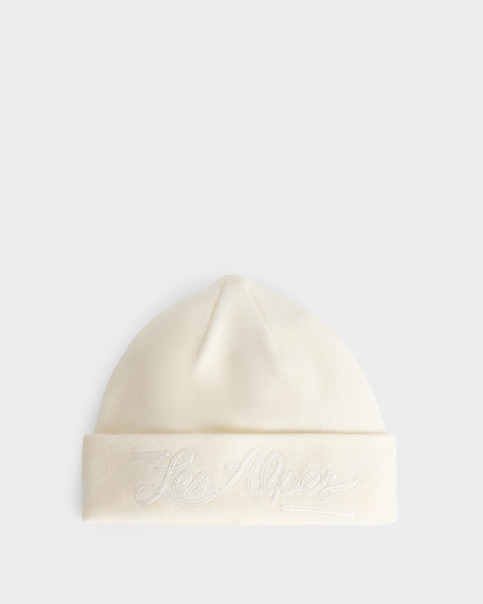 A white knit beanie, the ESTELLA - 8426521 Vanilla by Rudsak, with a folded brim and embroidered script text reading “Les Alpes,” displayed on a plain light background.