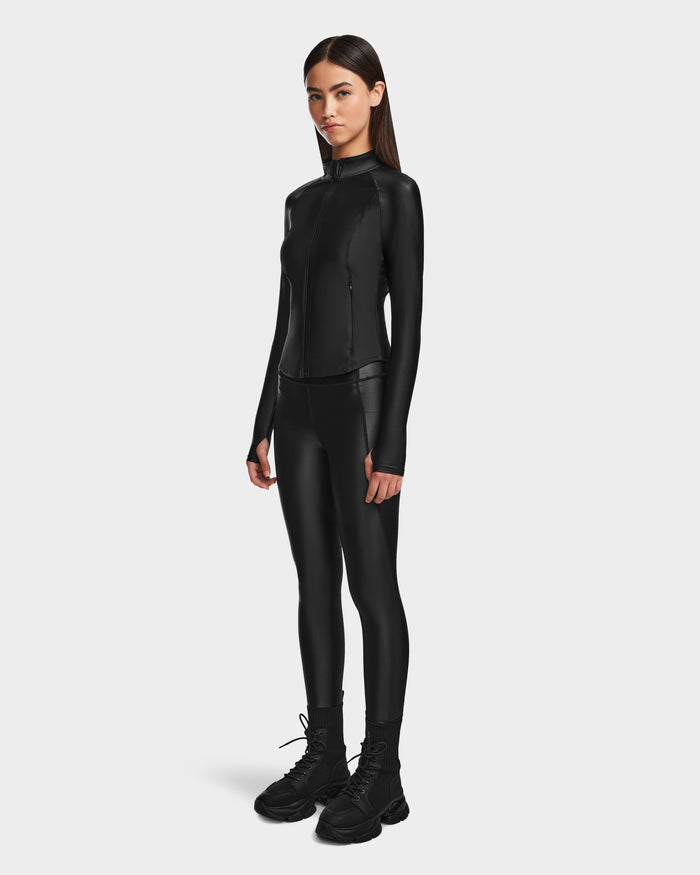 A woman faces forward against a white background, wearing the Rudsak EVA - 8524514 Black fitted zip-up top with a waterproof zipper, matching black leggings, and black lace-up boots.
