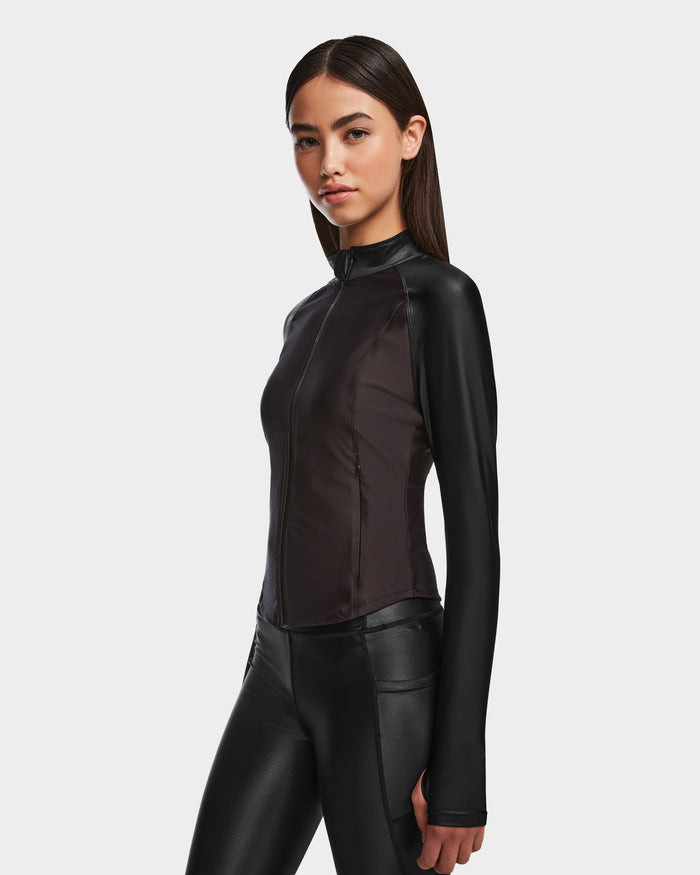 A woman with straight dark hair models the Rudsak EVA - 8524514 Black womens zip-up top and matching leggings in shiny stretch fabric, standing against a plain white background.