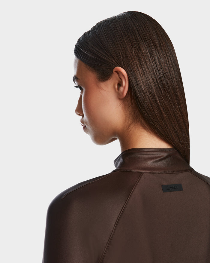 A person with straight, dark brown hair styled back is shown from behind at an angle, wearing Rudsaks EVA - 8524514 Espresso womens zip-up top in shiny stretch fabric with a small black label on the upper back against a plain background.
