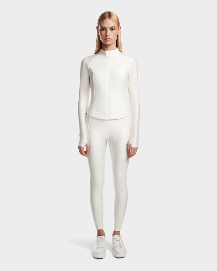 A woman with straight blonde hair faces forward, wearing Rudsaks EVA - 8524514 Iceland fitted zip-up top with a waterproof zipper, matching white leggings, and white sneakers against a plain light gray background.
