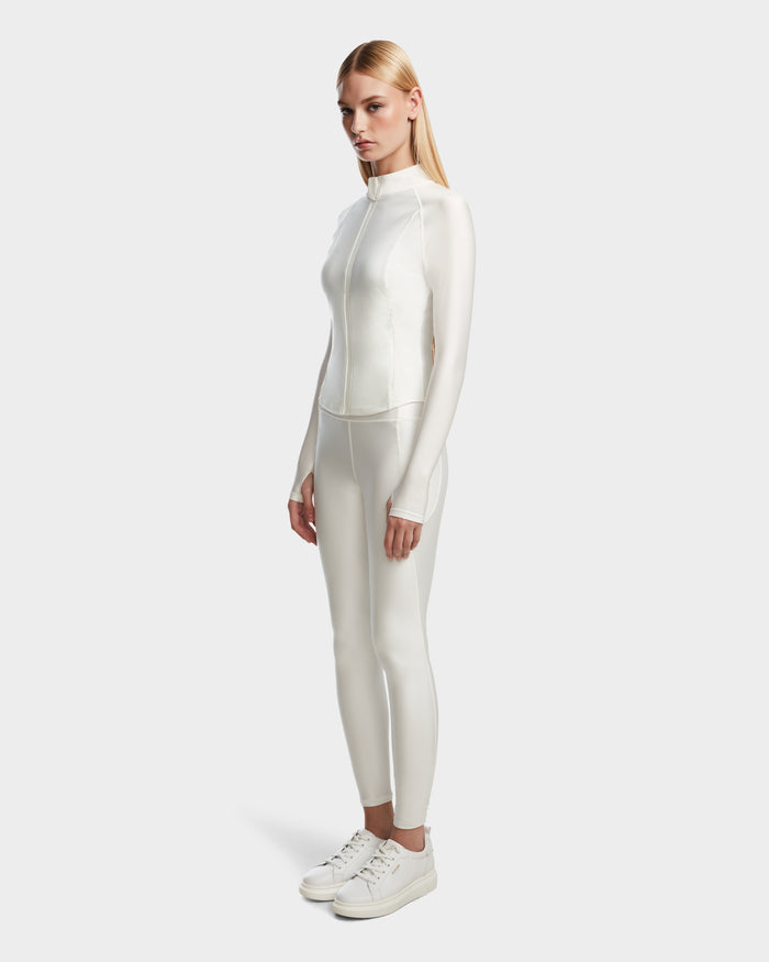 A woman with straight blonde hair models the Rudsak EVA - 8524514 Iceland fitted, long-sleeve women’s zip-up top and matching white pants with sneakers, posed against a plain light background.