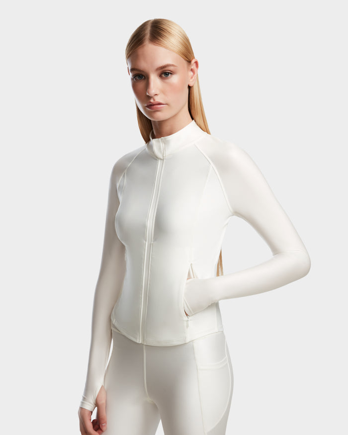 A woman with long, straight blonde hair models the Rudsak EVA - 8524514 Iceland fitted zip-up top and matching white leggings with a waterproof zipper, standing with one hand in her jacket pocket against a light background.