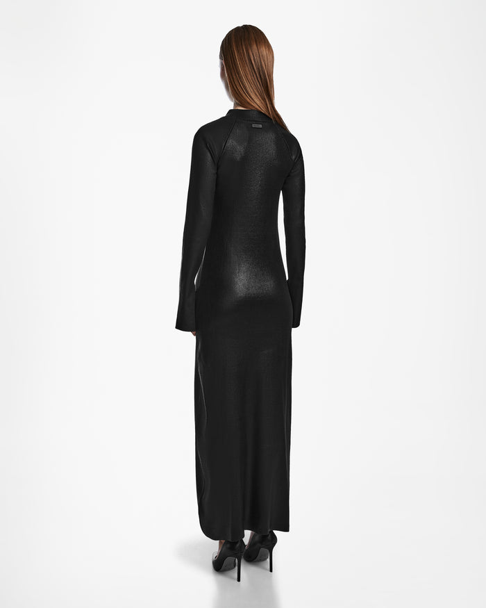 A woman with long brown hair stands facing away, wearing the Rudsak FAIZA - 8524579 Black maxi dress and black heels against a plain white background.