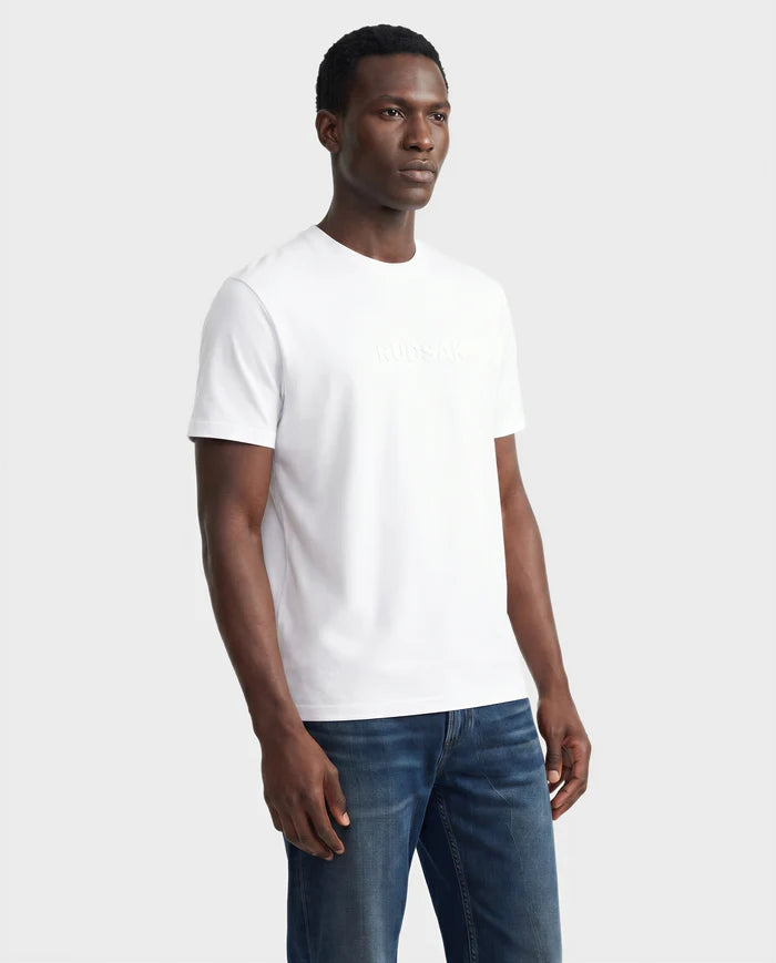 A man stands against a plain background, wearing the Rudsak FERDI - 6522005 t-shirt in natural white with subtle chest embossing and blue jeans. He faces slightly to the side with a neutral expression.