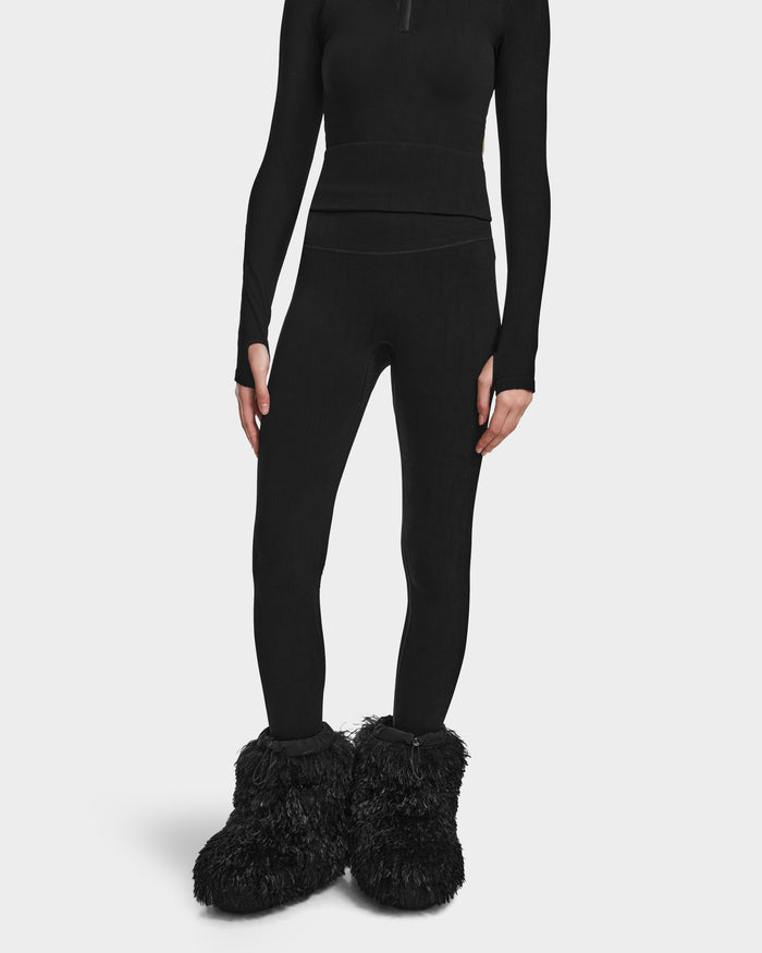 Someone models the FERKA - 8524542 Monogram Print Black leggings and a matching long-sleeve top from Rudsak, styled with large, fluffy black slippers. The persons head is not shown against the plain white background.