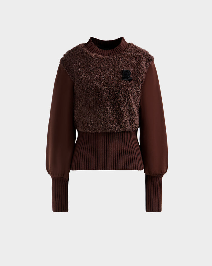 The FLORENCE - 8525546 Mocha by Rudsak is a brown women's long-sleeve faux fur top with a textured fuzzy front, ribbed cuffs and waistband, and a small black 'R' patch on the left chest. Set against a plain light gray background.