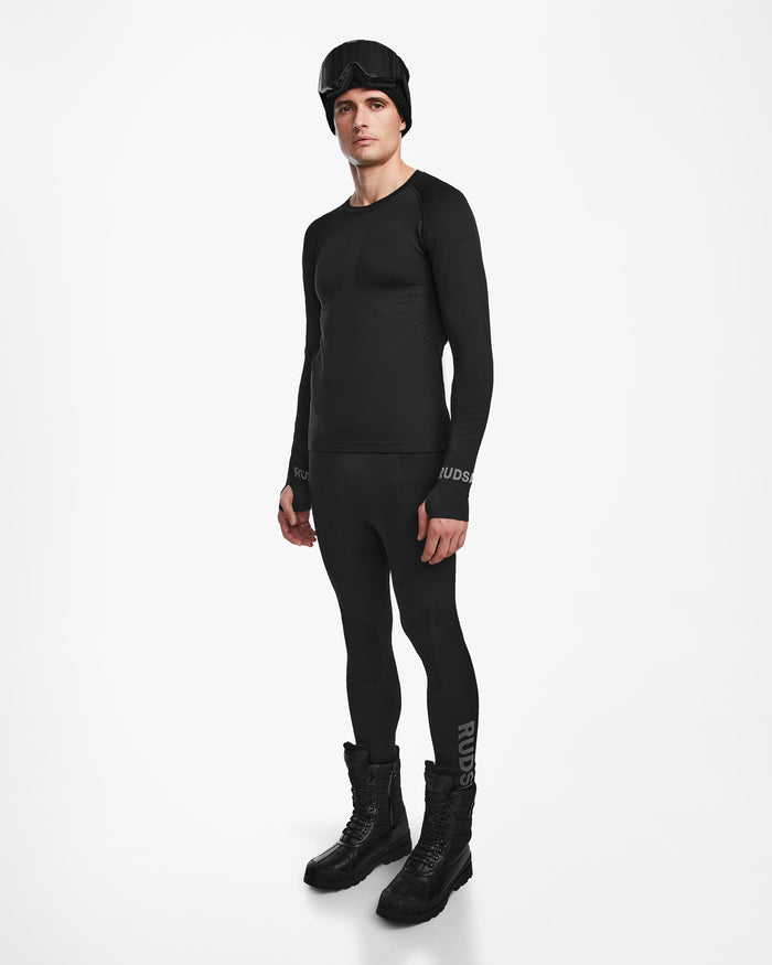 A man in the Rudsak FRANC - 6524541 Black men’s thermal base layer set, winter boots, and ski goggles stands against a white background.